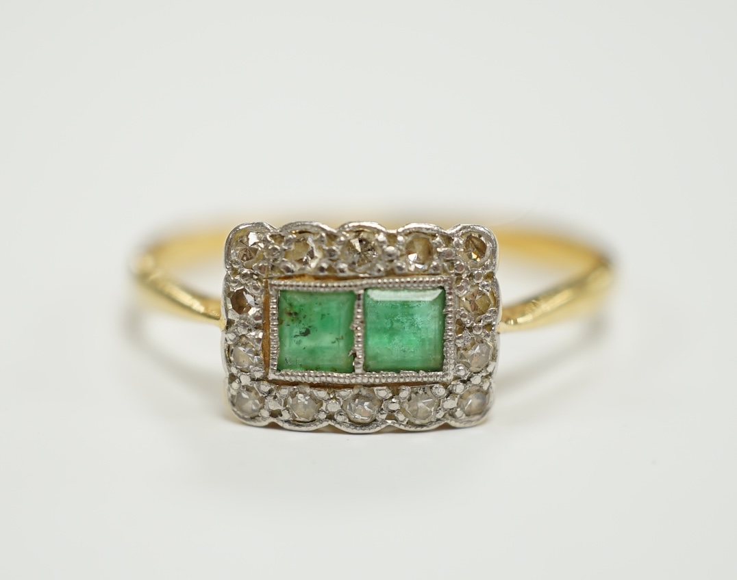 An 18ct, two stone emerald and diamond cluster set tablet ring, size M/N, gross weight 2.2 grams.